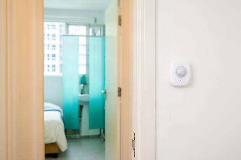 Discreet wall-mounted motion sensor beside a bathroom doorway in a bright Singapore HDB flat